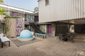 Une cour dotée d’un espace aménagé avec des sièges, d’une grande sculpture bleue et d’un escalier menant à un niveau supérieur.