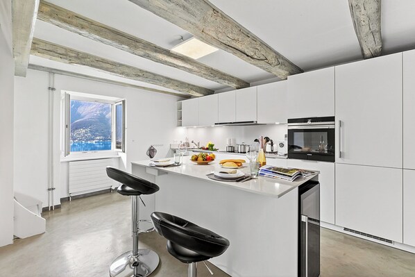 Une cuisine moderne avec des meubles blancs, un îlot central et une grande fenêtre donnant sur un paysage montagneux.