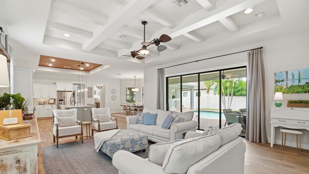A spacious living room with a large sofa, a coffee table, and a dining area. There is a kitchen in the background and a sliding glass door leading to a pool area. - Family Beach Oasis w/ Heated Pool, Spa & Guest House (Bonita Springs)