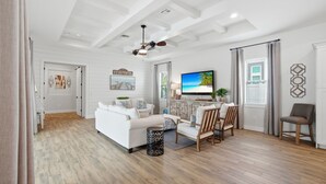 A spacious living room with a white sofa, a dining area with chairs, a TV, and a ceiling fan. - Family Beach Oasis w/ Heated Pool, Spa & Guest House (Bonita Springs)
