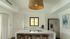 Una cocina moderna con una isla central, taburetes de bar, un refrigerador y una lámpara colgante.