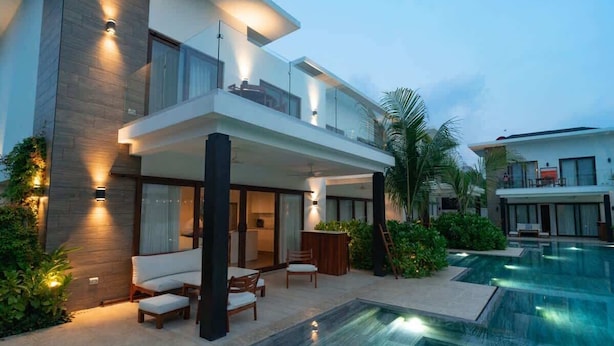 Una casa moderna de dos pisos con piscina, mobiliario de exterior y un jardín bien cuidado.