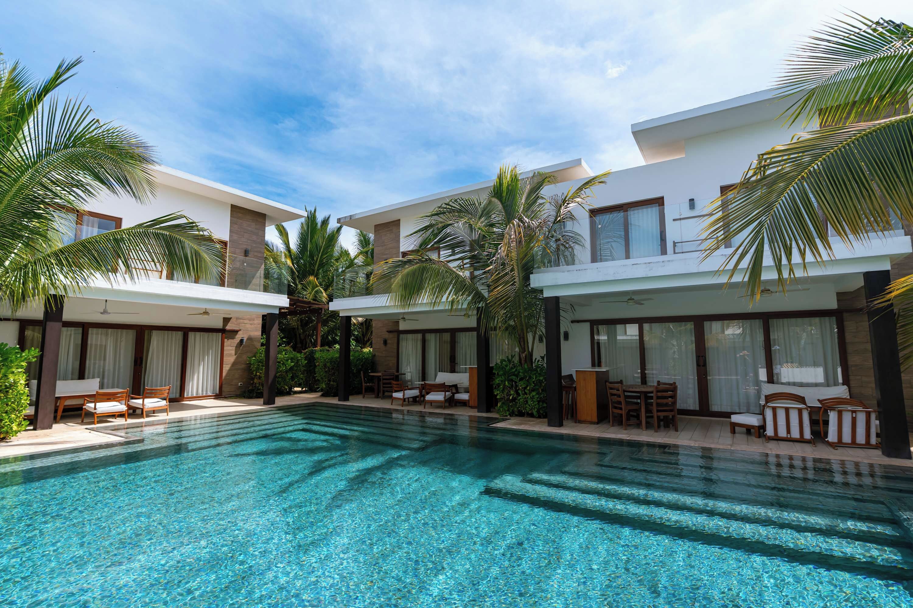 A modern hotel with a central swimming pool, outdoor seating, and palm trees.