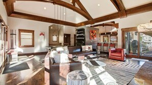Un espacio habitable amplio con techo alto y vigas a la vista, un ventanal grande y una disposición de asientos que incluye sofás y una silla roja.