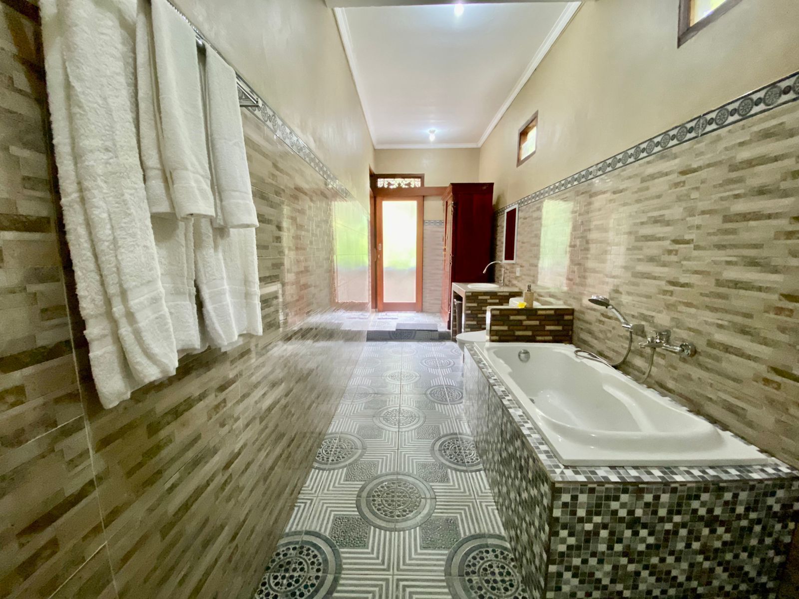 A bathroom with a large bathtub, a sink, and a mirror. There are towels hanging on the wall and a patterned floor.
