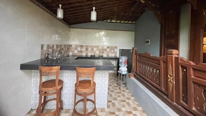 Une cuisine avec un coin bar, deux tabourets de bar en bois, un distributeur d’eau et une rambarde en bois.