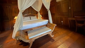 Un lit à baldaquin à quatre poteaux, avec un banc en bois, dans une pièce rustique aux murs et au plafond en bois.