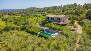 Une maison en pierre avec une piscine, entourée d’oliviers.