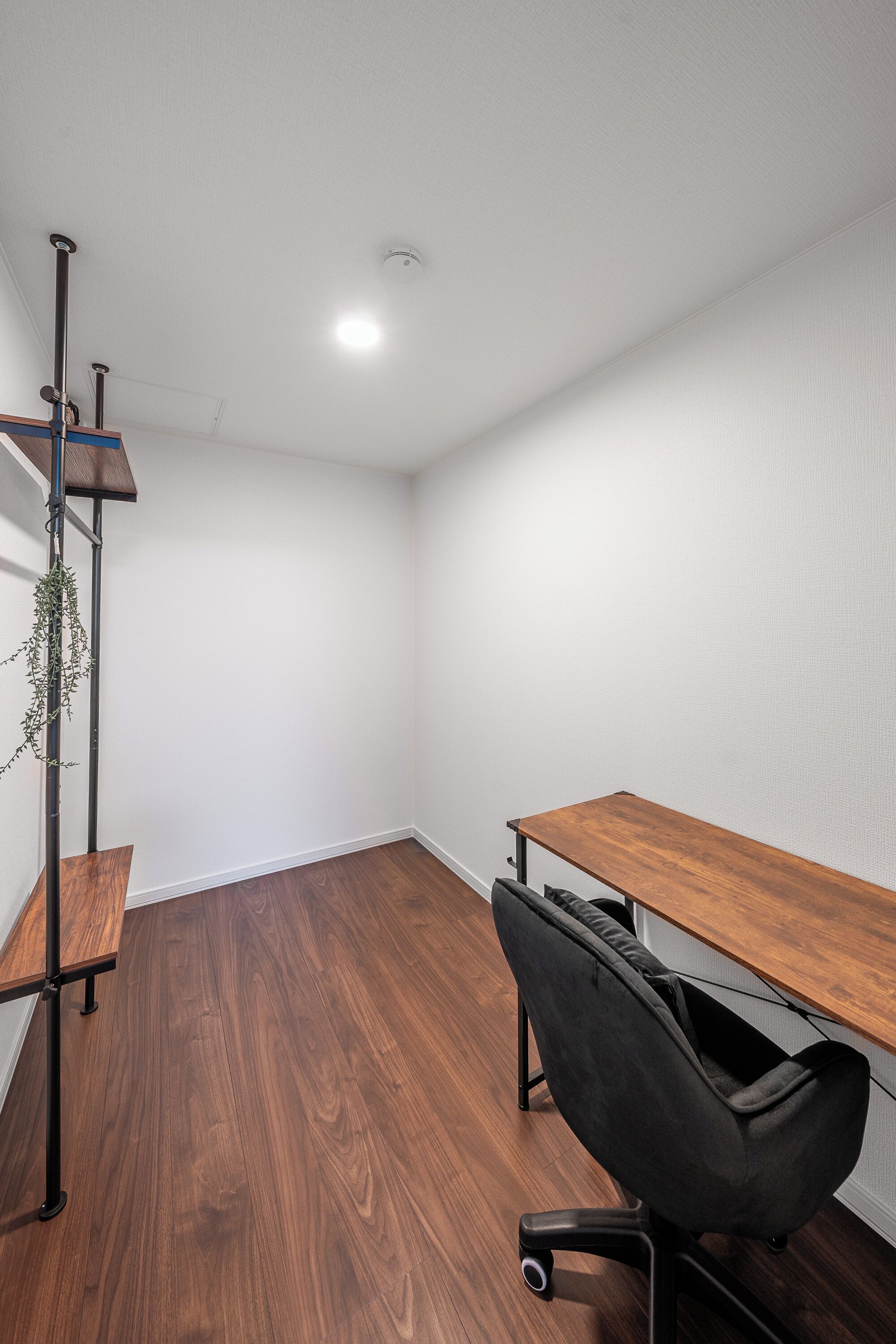 A room with a wooden desk, black office chair, and a metal shelving unit with a plant.