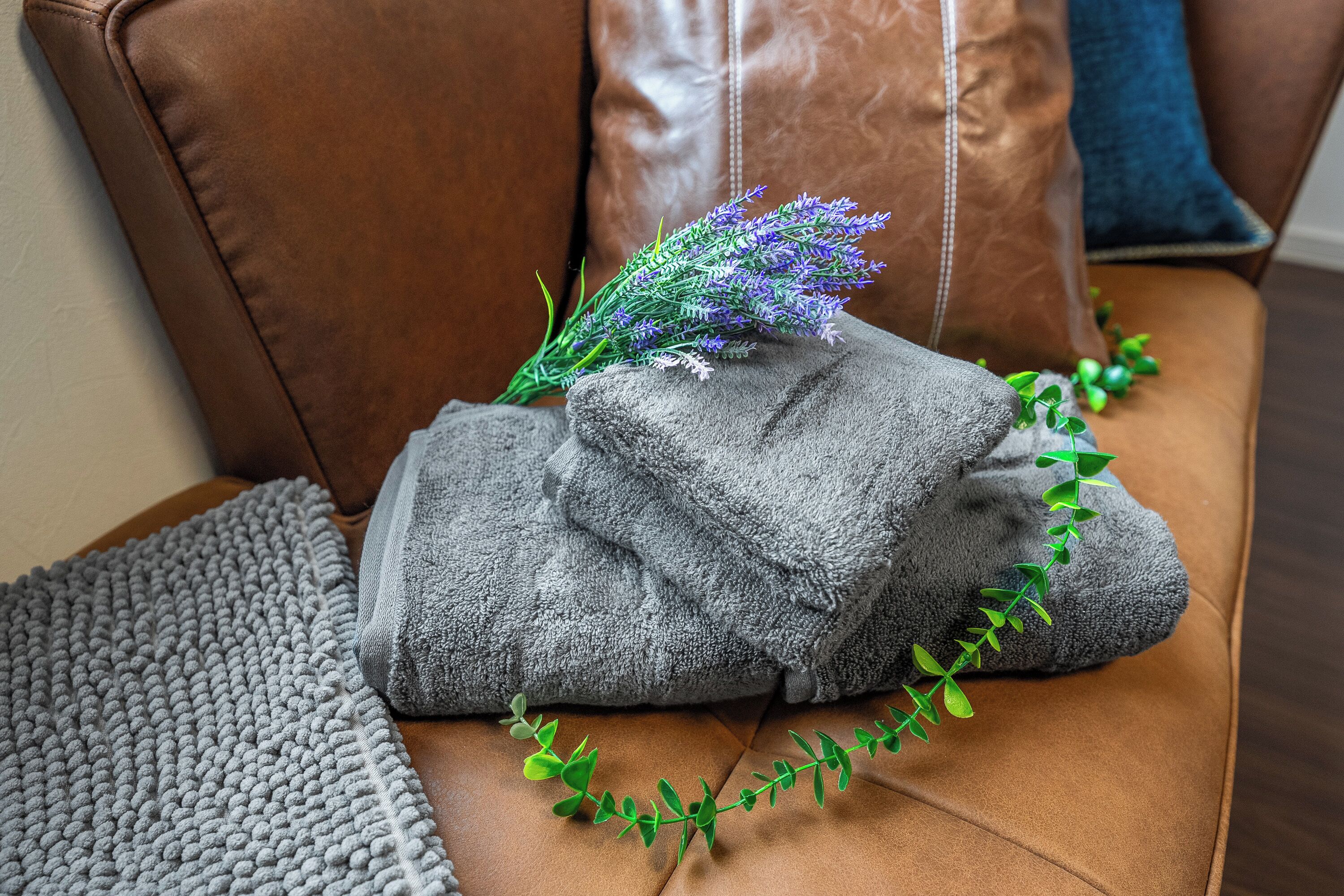 A brown leather sofa with folded gray towels and a sprig of lavender.