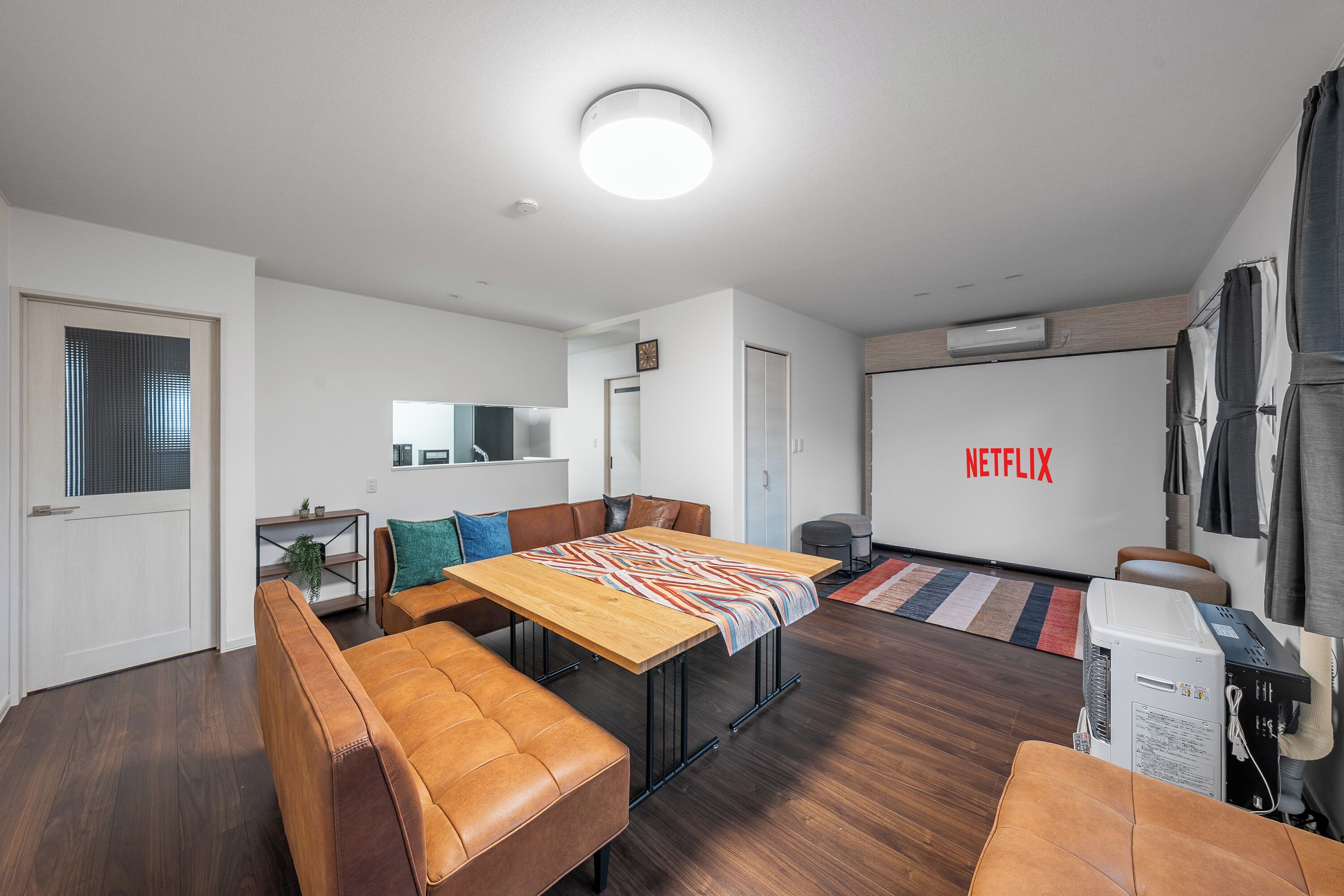 A modern living room with a wooden dining table, leather sofas, and a large TV screen displaying the Netflix logo.