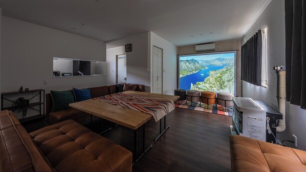 A modern living room with a wooden dining table, leather sofas, a large window with a mountain view, and a ceiling-mounted projector. - CALM FOREST (Asahikawa)