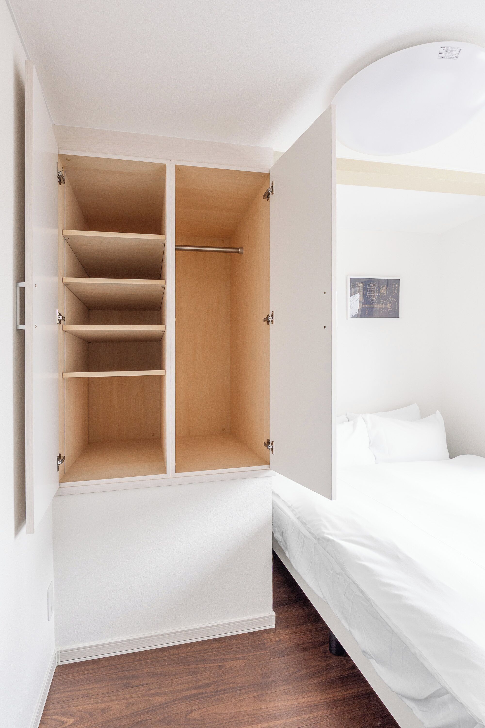Ein Schlafzimmer mit einem Bett, einem Holzschrank mit Einlegeböden und einer weißen Wand.
