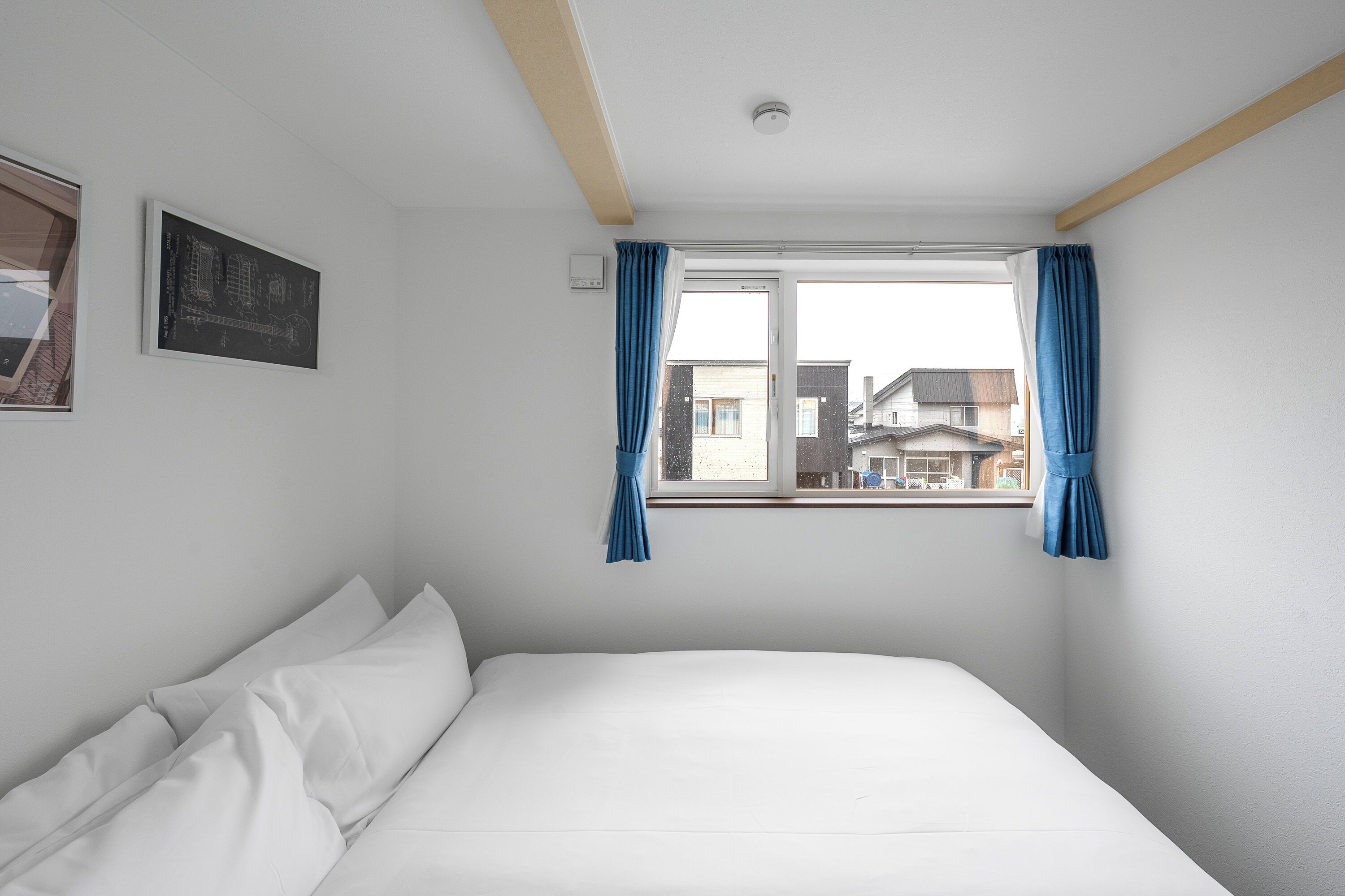 Un dormitorio con cama, ventana con cortinas, luz empotrada en la pared y un cuadro enmarcado.