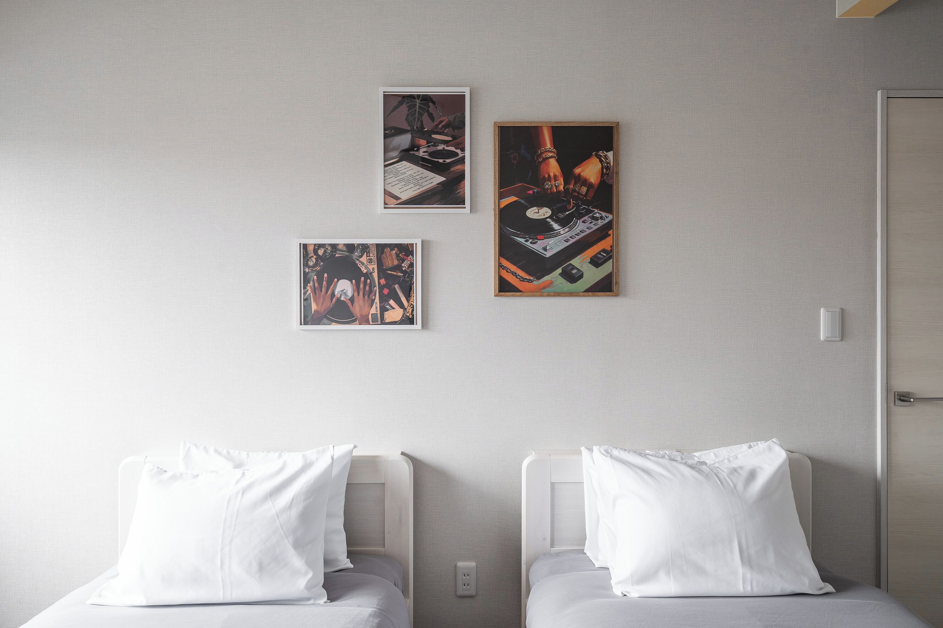Habitación de hotel con dos camas individuales, un enchufe en la pared y tres cuadros con imágenes de equipo de DJ y personas.