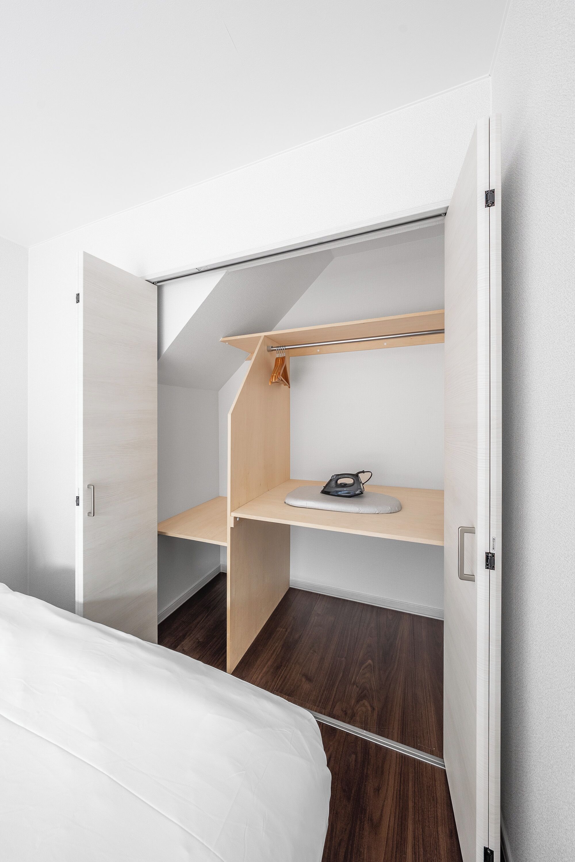 A compact bedroom with a built-in wardrobe, a small desk, and a hanging rack.