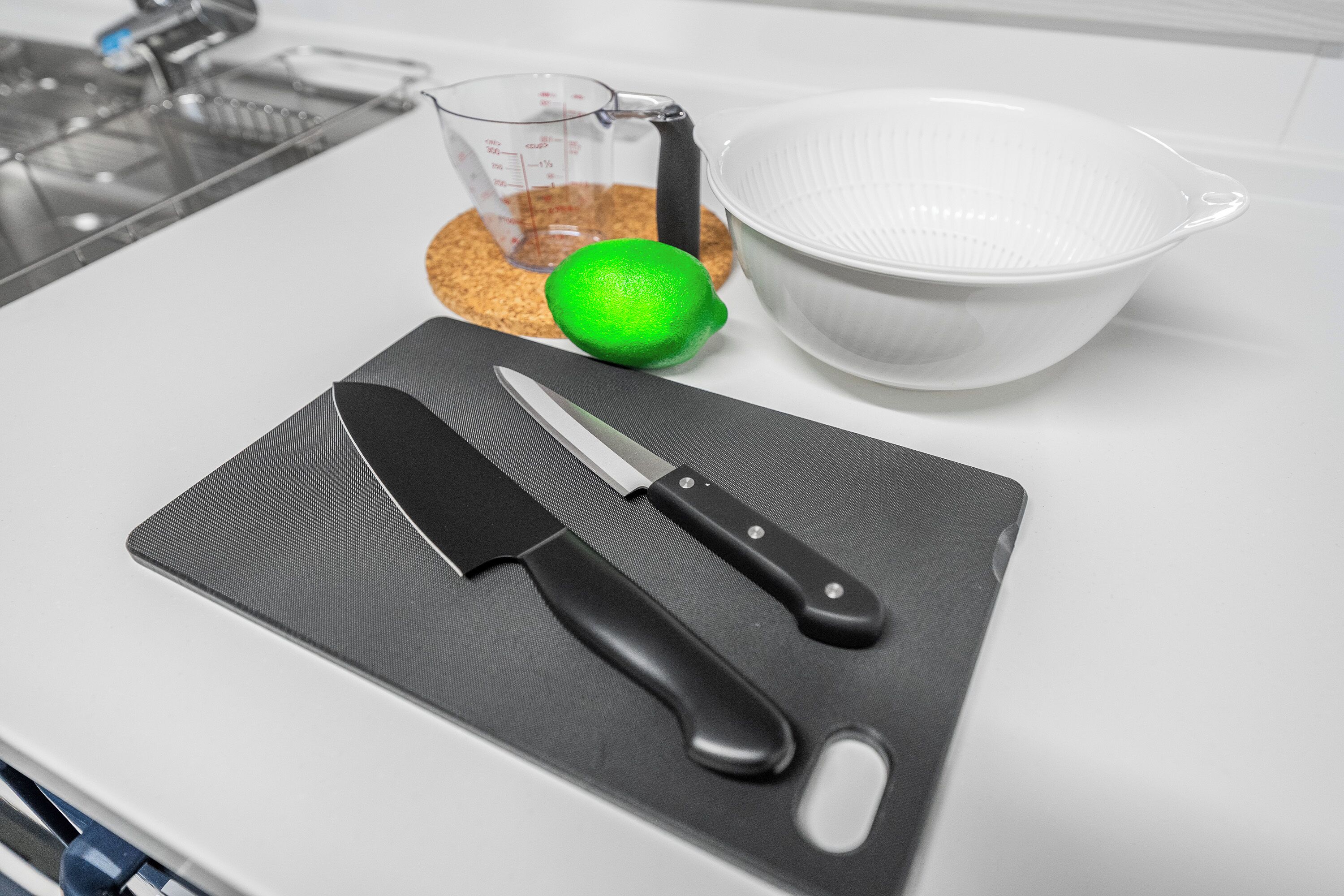 Una encimera de cocina con tabla de cortar, un cuchillo, una taza medidora, un bol y un limón.
