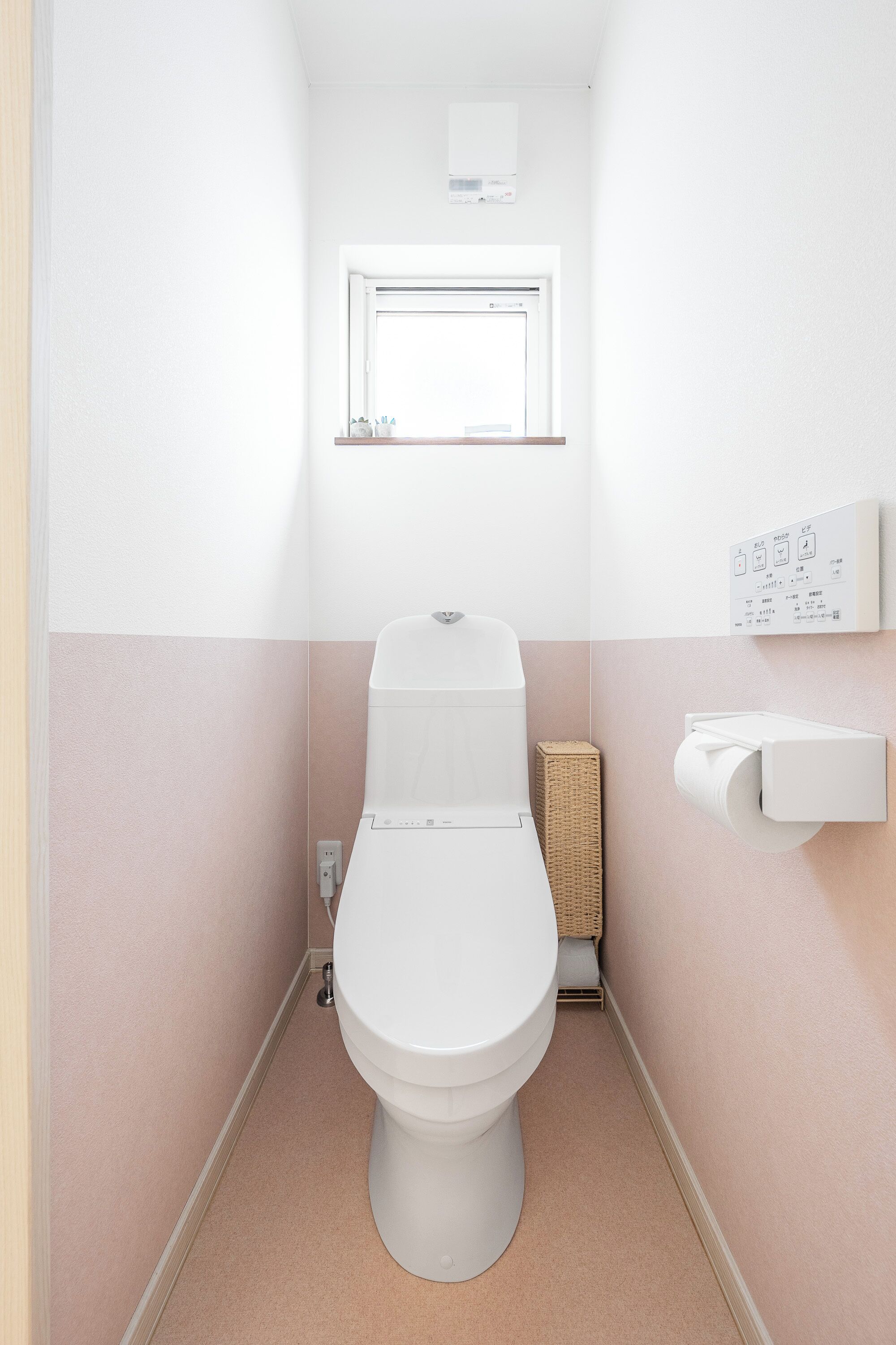 A small, modern bathroom with a toilet, a wall-mounted toilet paper holder, and a window above the toilet.