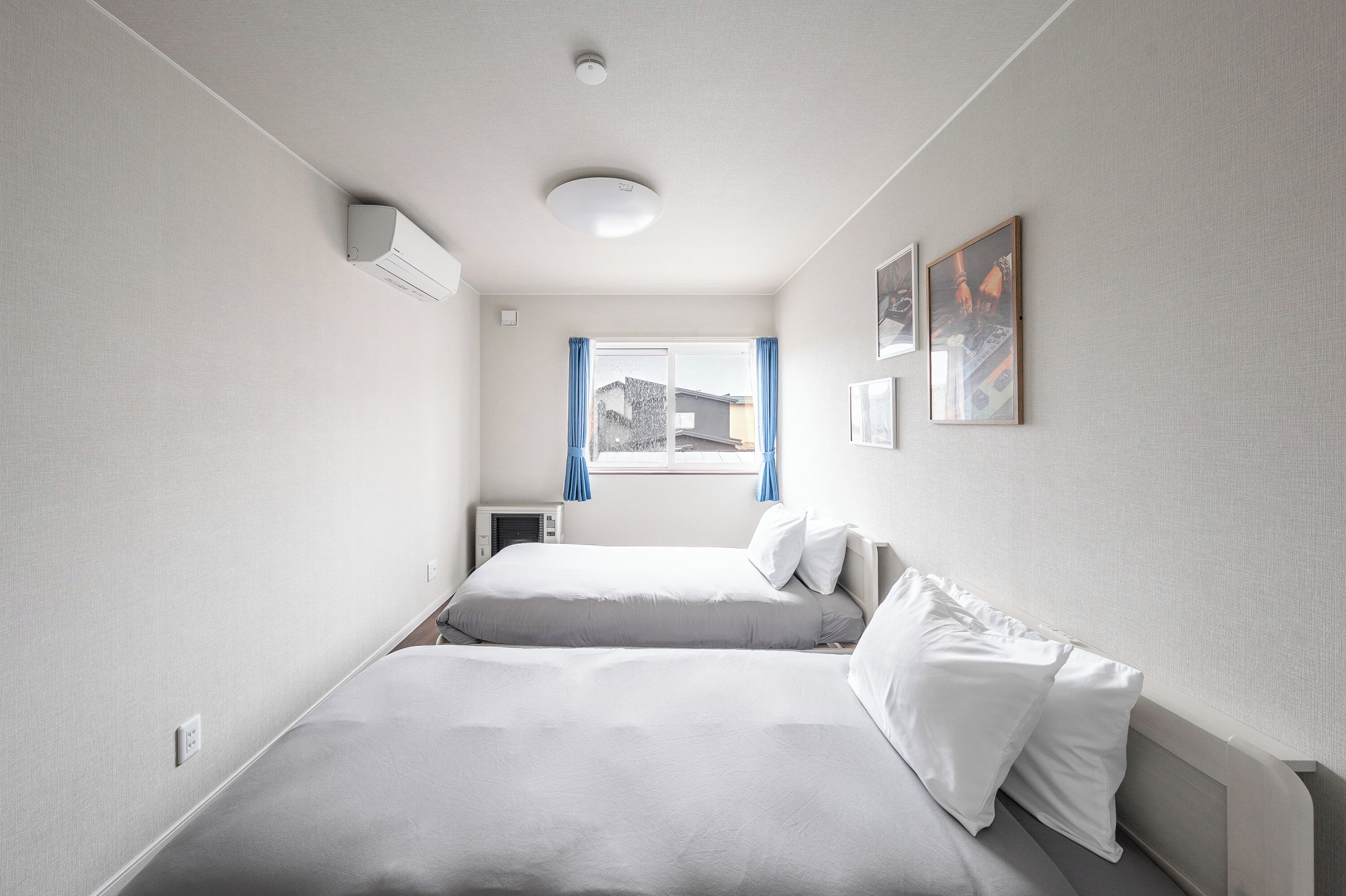 Una habitación con dos camas, una ventana con cortinas azules y una lámpara en el techo.