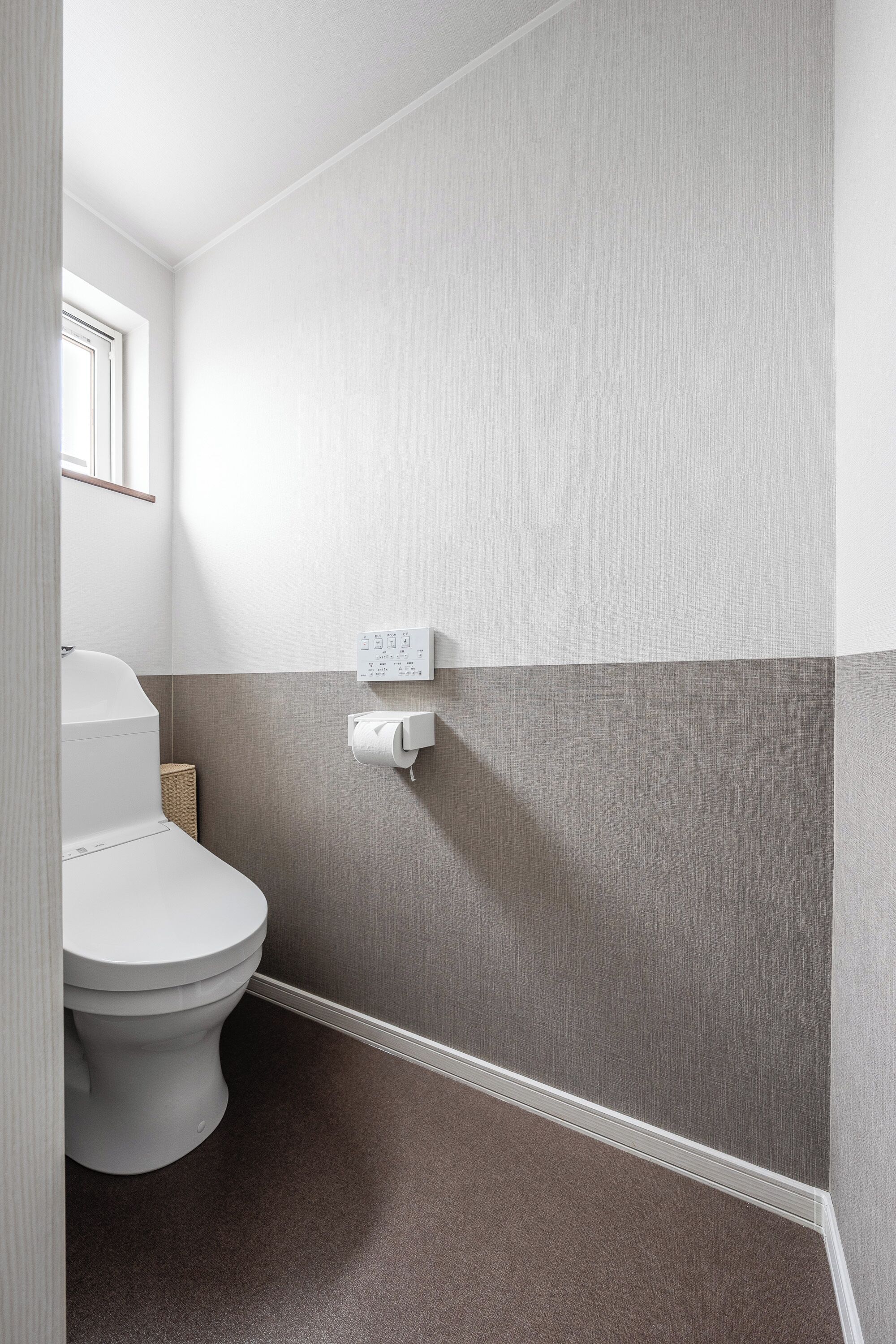 A bathroom with a toilet, a towel dispenser, and a wall-mounted light switch.