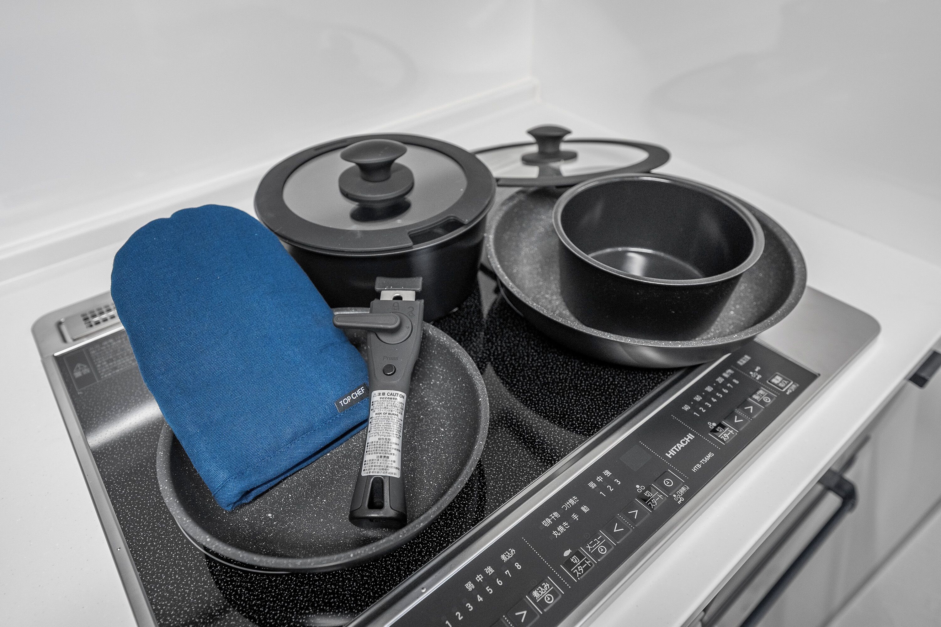 A kitchen with a stove, pots, and a blue oven mitt.