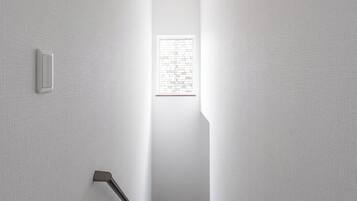 A narrow, well-lit hallway with a wooden staircase leading to a room with a window.
