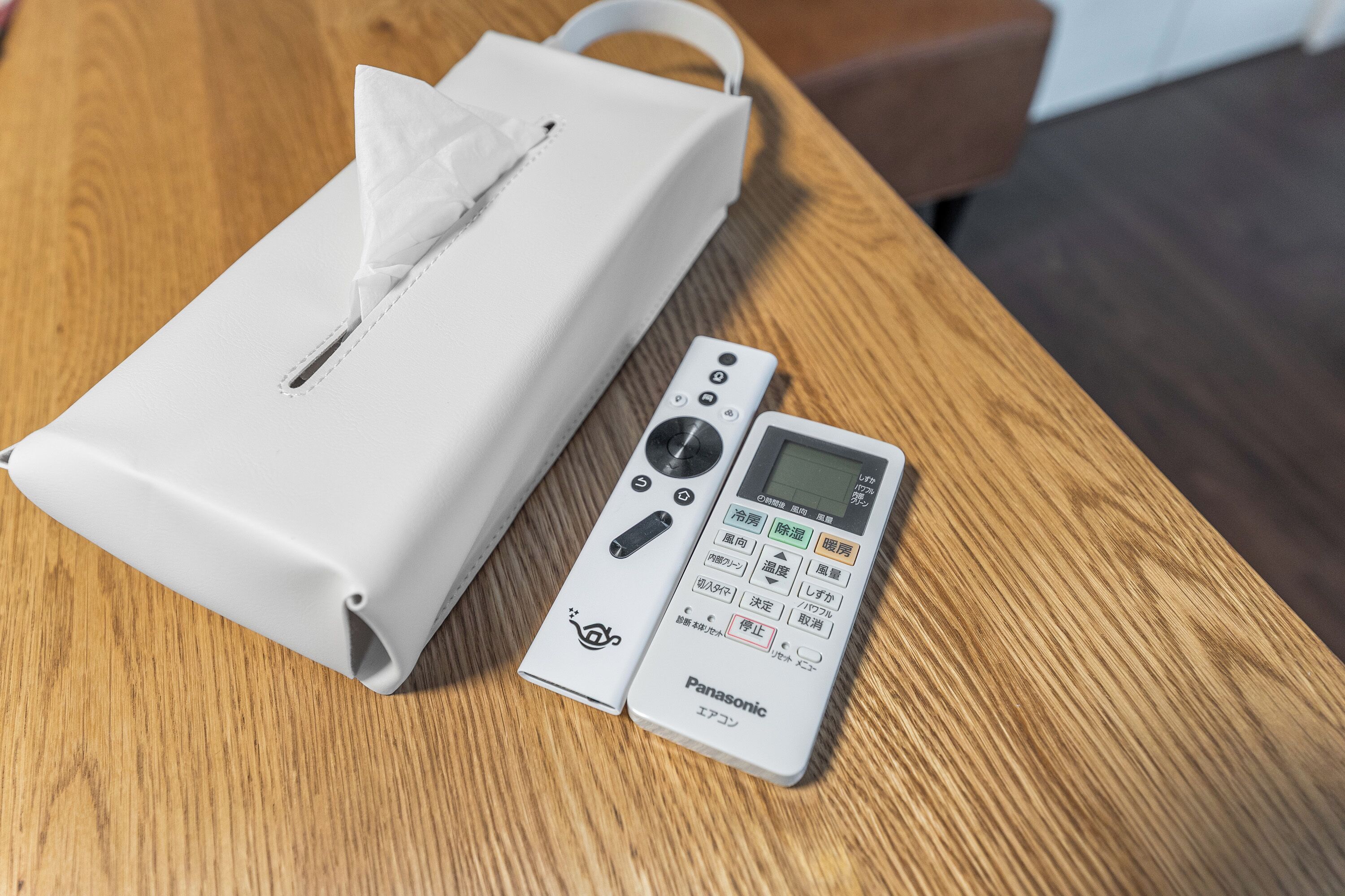 A tissue box and a Panasonic remote control on a wooden table.