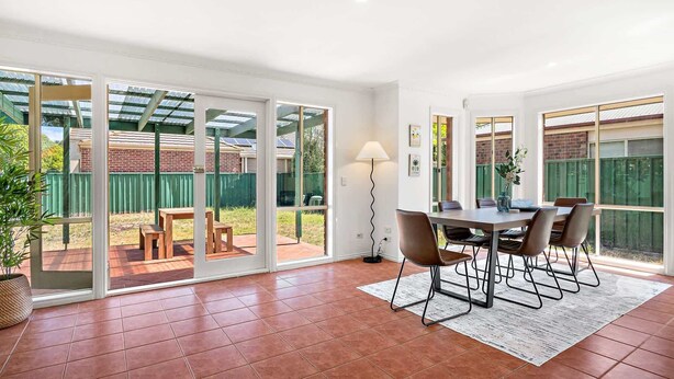 Ein großzügiger Patio-Bereich mit Esstisch und Stühlen, einer Stehlampe und Blick auf den Garten durch große Schiebetüren.