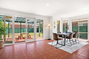 Un vaste patio comprenant une table et des chaises, un lampadaire et une vue sur le jardin à travers de grandes portes-fenêtres coulissantes.