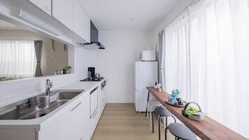 A modern kitchen with white cabinets, a stainless steel sink, a wooden dining table with bar stools, and a refrigerator.