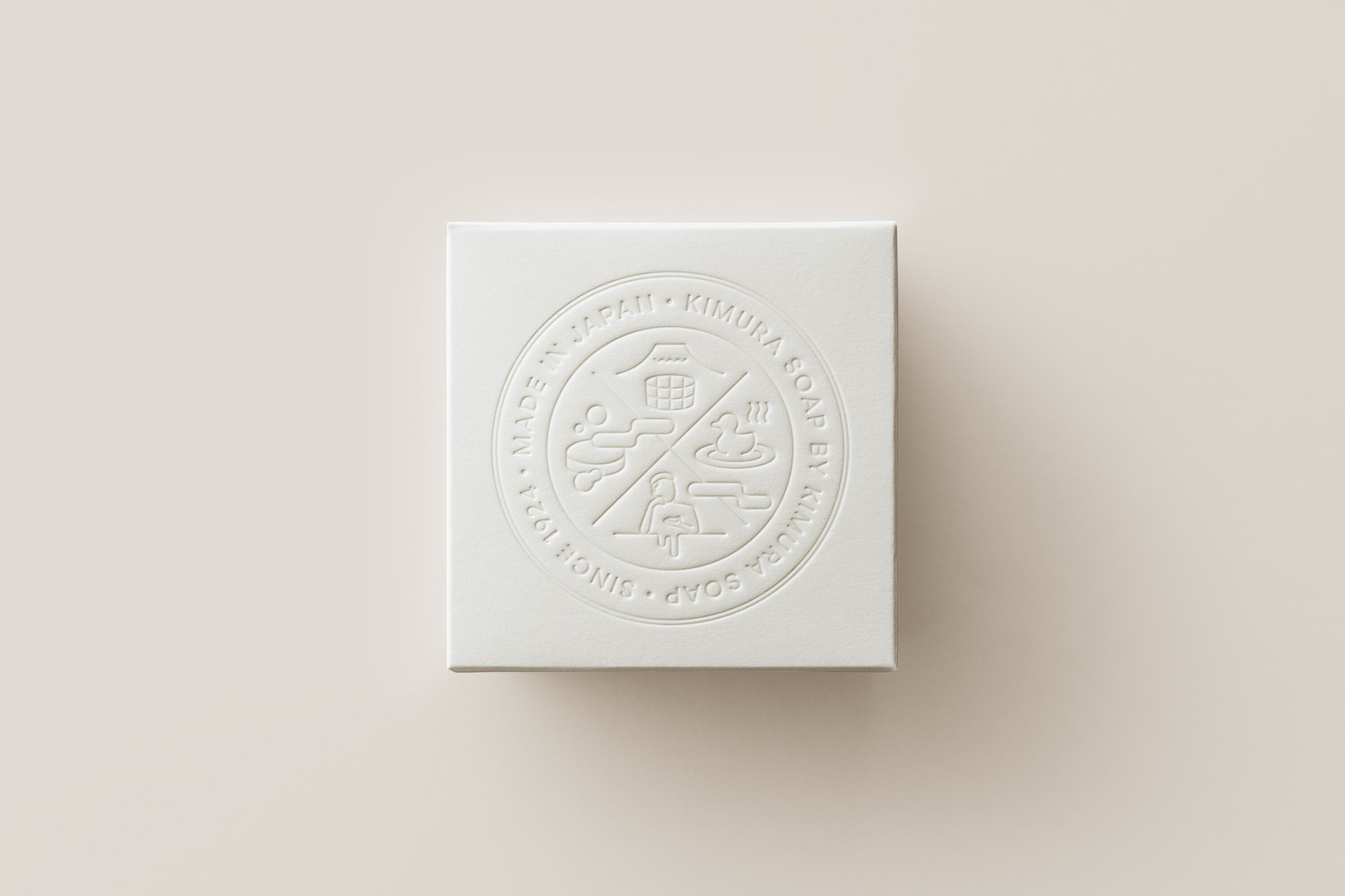 Een wit vierkant voorwerp met opdruk van tekst en symbolen, waaronder 'MADE IN JAPAN' en 'KIMURA SOAP'.