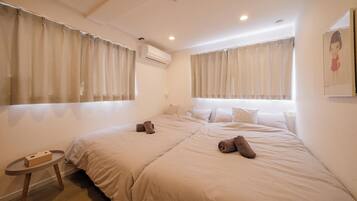 A hotel room with two beds, a small round table, and a wall-mounted air conditioner.