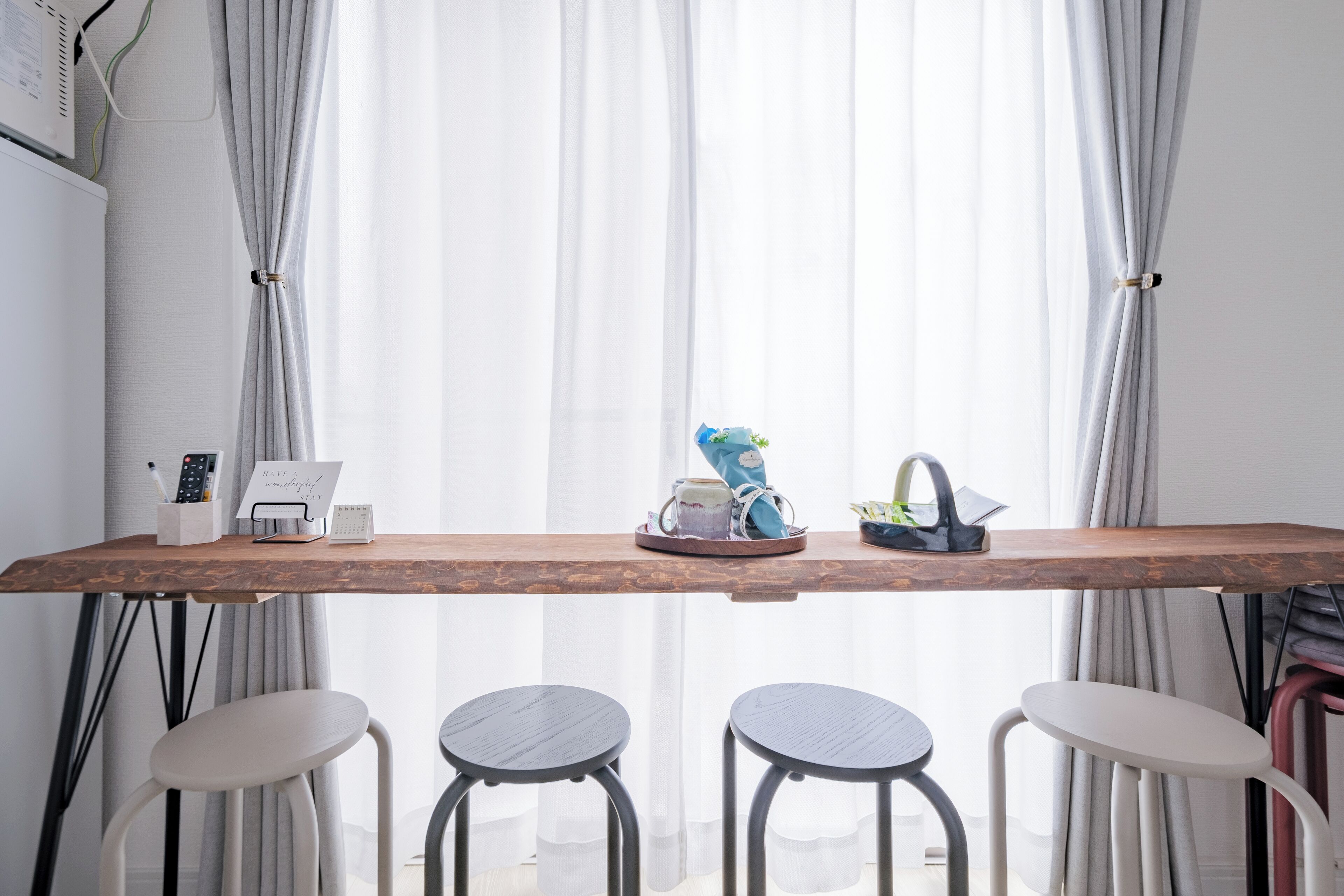 A wooden table with a remote control, a calendar, and a small plant. There are three stools in front of the table.