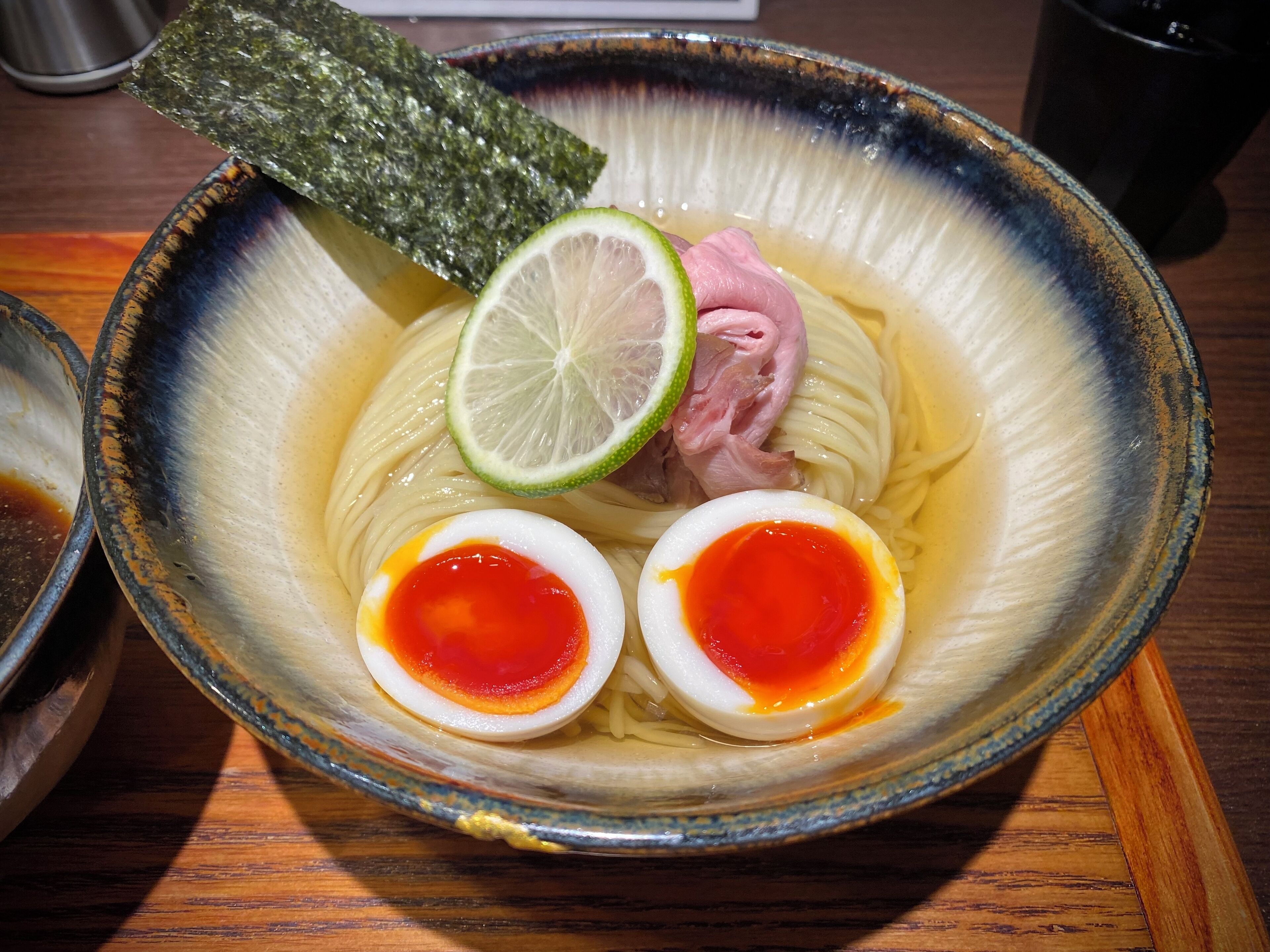 A bowl of ramen with a slice of lime and a piece of seaweed on the side.