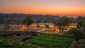 Una serie de cabañas pequeñas y uniformes con un espacio común central, rodeadas de campos abiertos y árboles, durante el atardecer.
