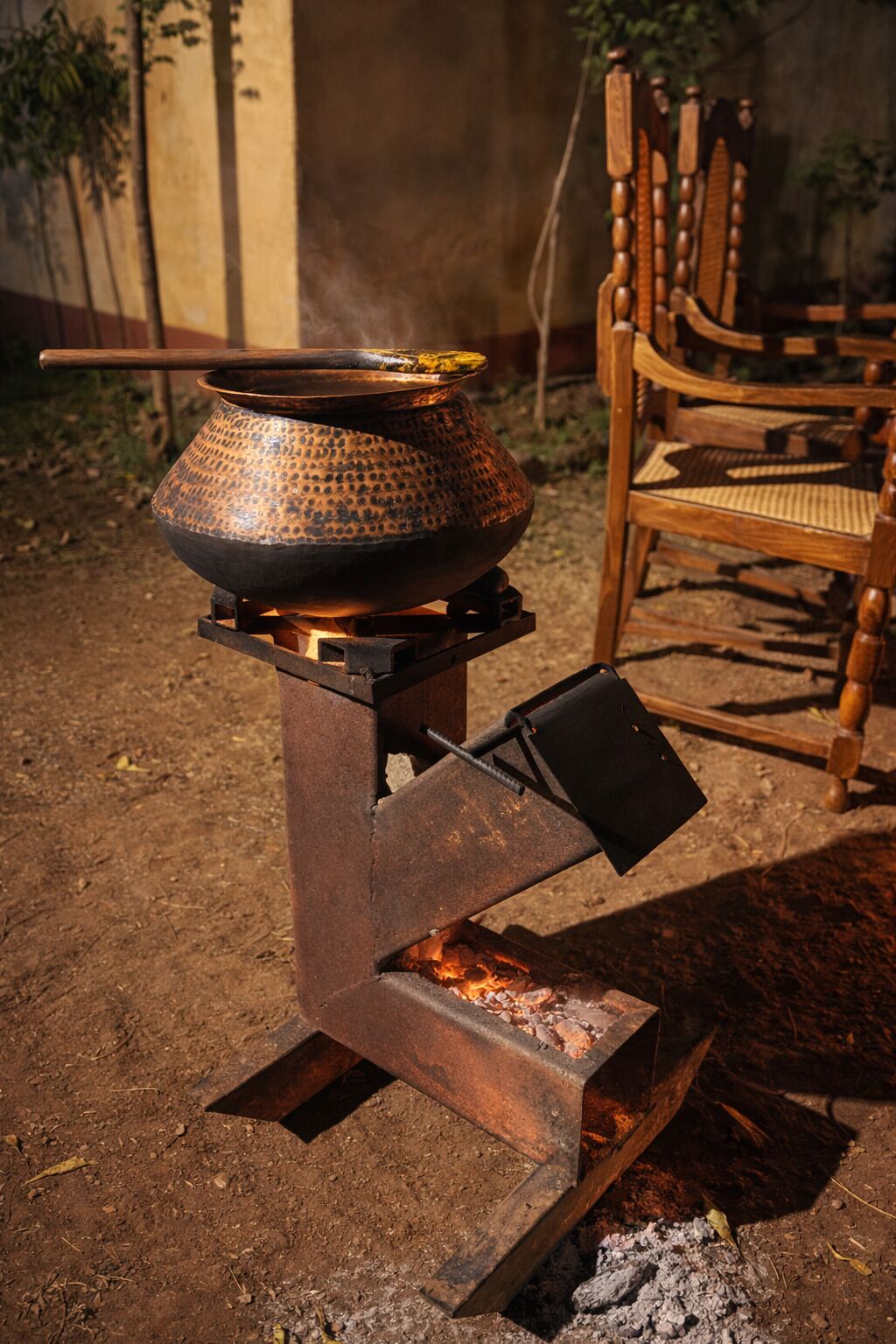 A rustic outdoor cooking setup with a metal stove and a pot on a stand.