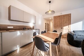 A modern kitchen with a wooden dining table and chairs, a hanging light fixture, and a built-in wooden cabinet. - CHALET PASCAL C03: New 3 bedrooms + cabin for 6 people (MORZINE)