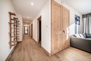 A hallway with wooden flooring, a built-in wooden shelf, a large wooden door, and a grey sofa. - CHALET PASCAL C03: New 3 bedrooms + cabin for 6 people (MORZINE)