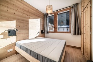 A wooden-paneled room with a bed, a hanging light fixture, a window with curtains, and a view of a building outside. - CHALET PASCAL C03: New 3 bedrooms + cabin for 6 people (MORZINE)