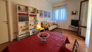 Een woonkamer met een rode tafel, een bank, een televisie en een boekenplank.