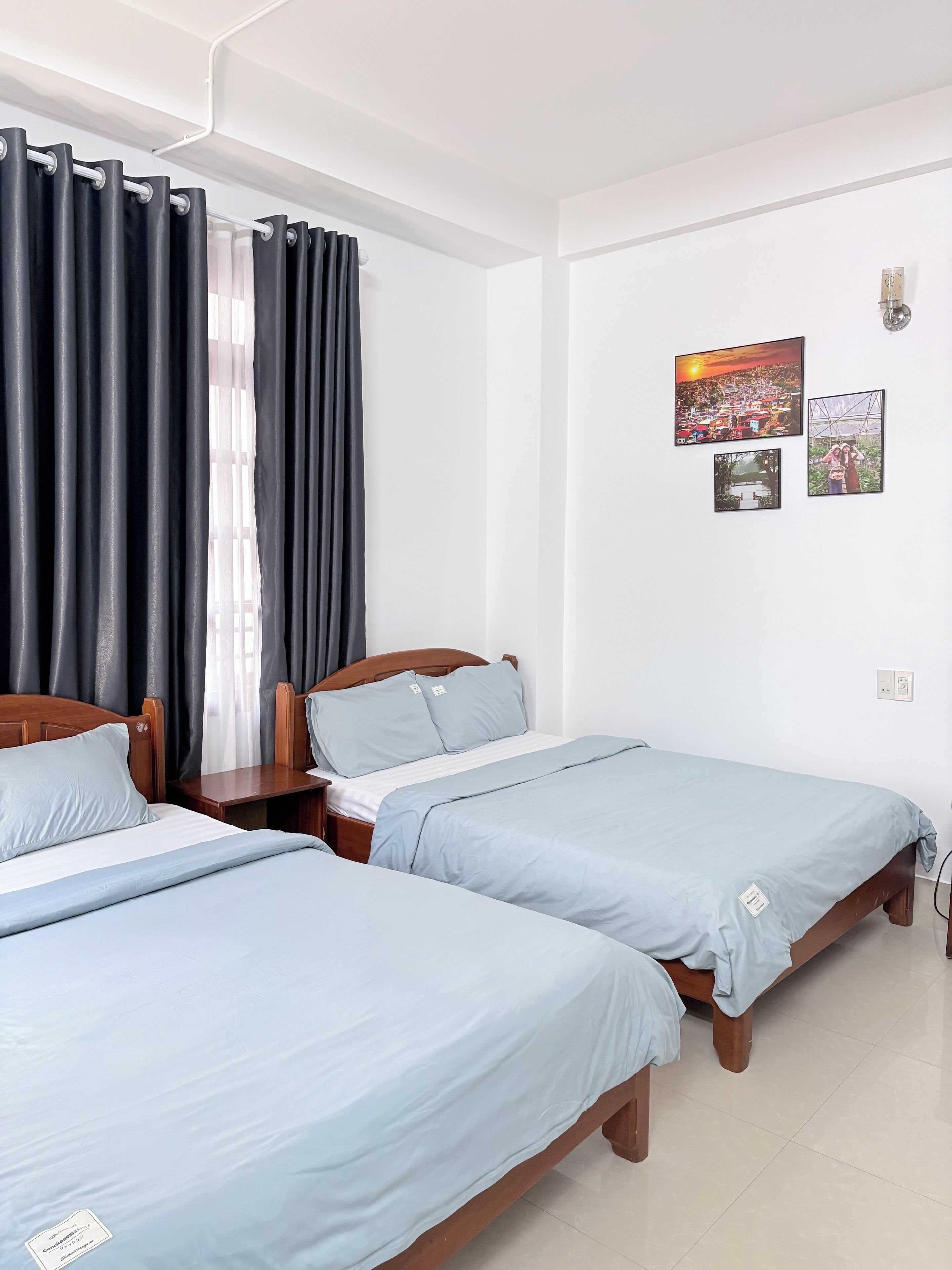 A hotel room with two beds, a wooden headboard, a nightstand, and a wall with framed pictures.