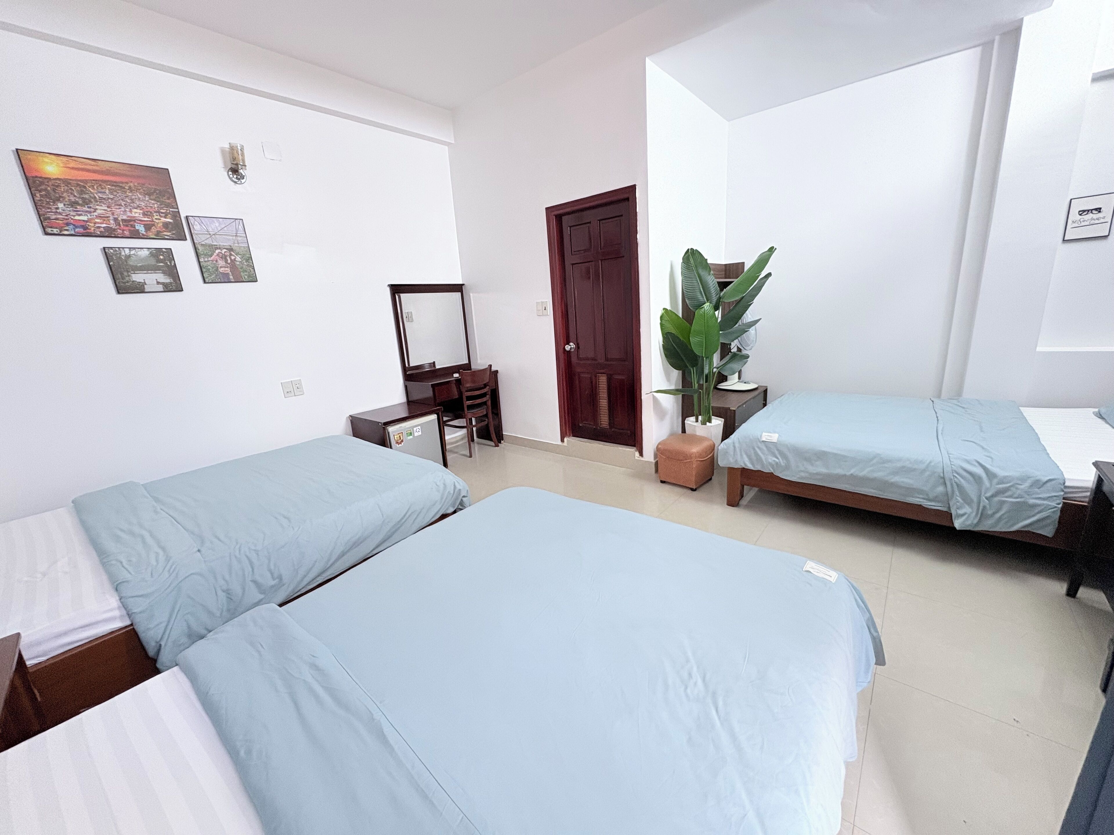 A bedroom with two single beds, a desk with a chair, a mirror, and a potted plant.