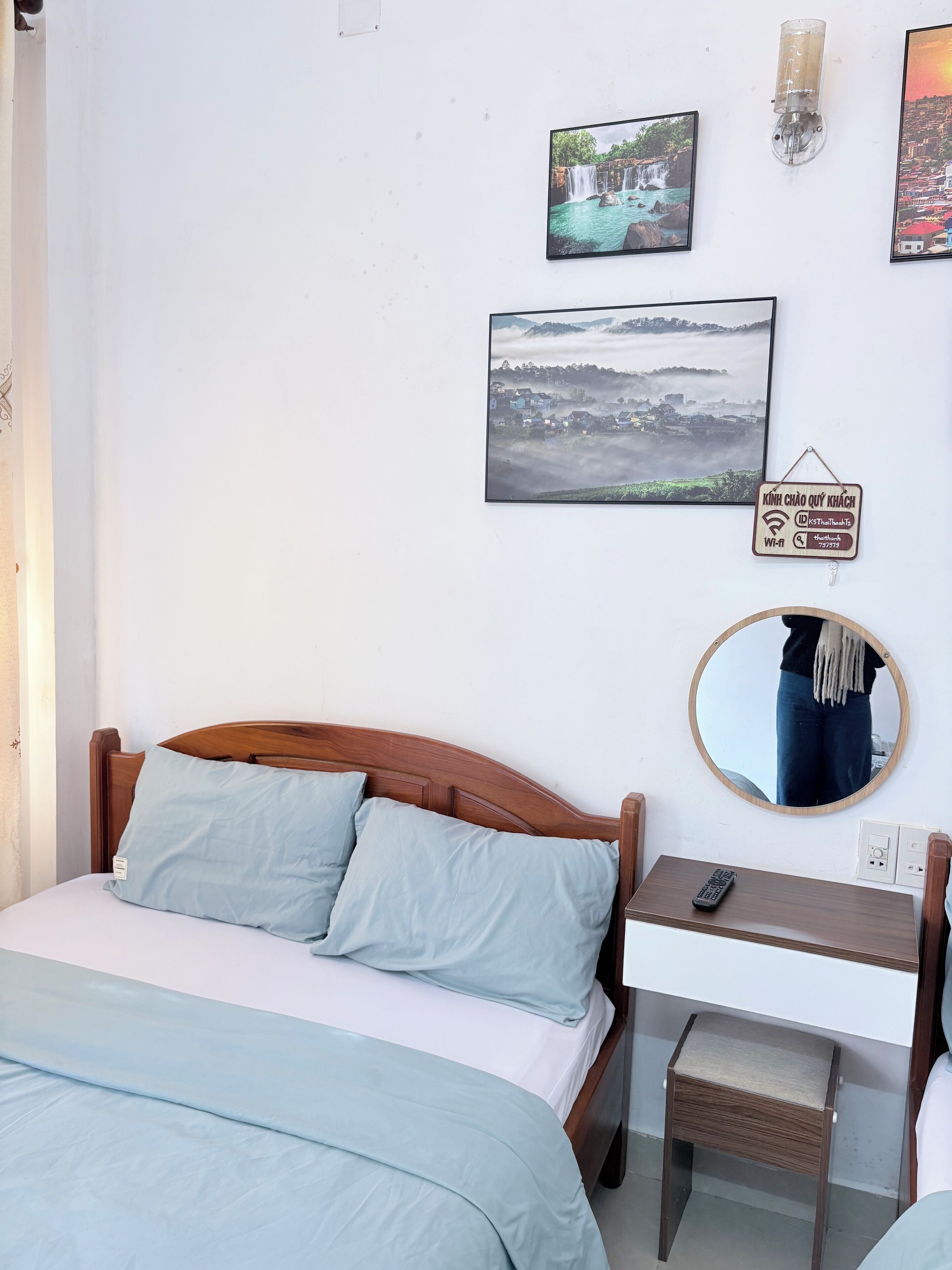 A bedroom with a wooden bed, a bedside table with a mirror, and two framed pictures on the wall.