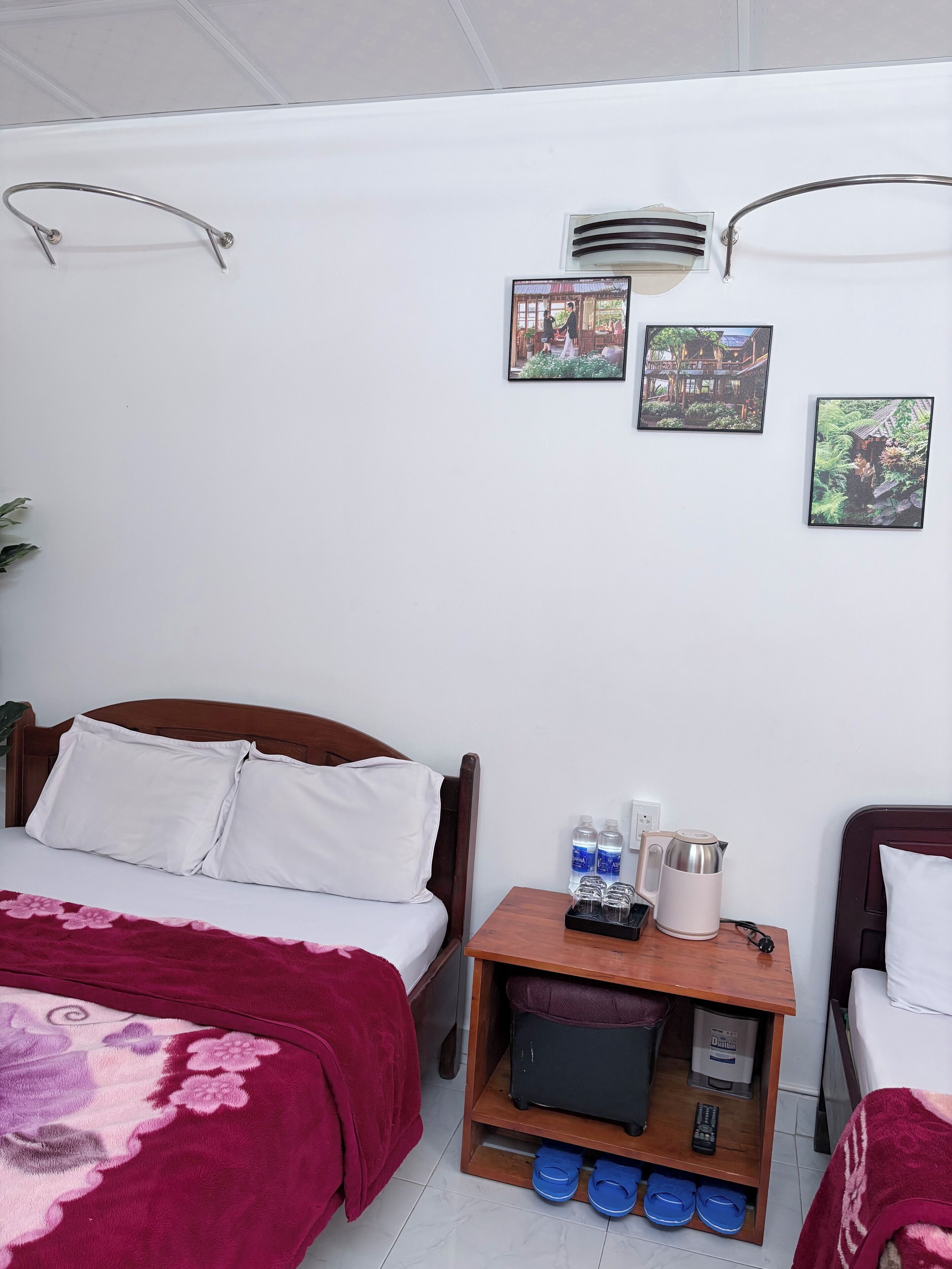Ein Hotelzimmer mit einem Bett, einem Nachttisch aus Holz mit einem Wasserkocher, einem Fernseher und einem kleinen Regal mit Hausschuhen.