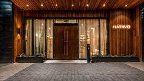 Ein moderner Gebäudeeingang mit Holzfassade, einer großen Glastür mit der Zahl '48' darüber und einem Neon-Schild mit der Aufschrift 'NATIVO'.