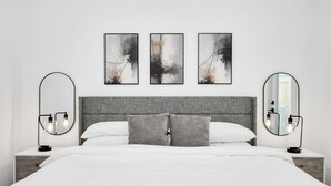 A modern bedroom with a grey headboard, white bedding, and two bedside tables with round mirrors and wall sconces. - Modern 3 Bedroom Close To DTWN/NRG/Med Center (Houston)