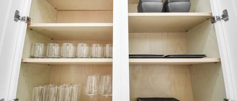 A cabinet with shelves containing clear glasses and a black wallet.