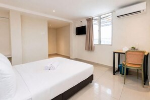 Ein Hotelzimmer mit einem Bett, einem Schreibtisch mit Stuhl, einem Fernseher und einer Klimaanlage.