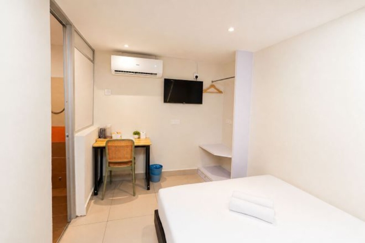 Una stanza piccola e pulita con un letto, una scrivania, una sedia, una TV e un condizionatore d'aria.