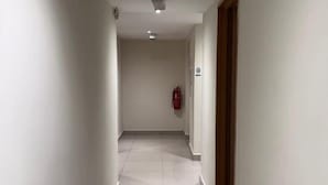 A hallway with white walls and a tiled floor, leading to a door with a fire extinguisher mounted on the wall. - Swing & Pillows @ Kajang Selangor (Kajang)